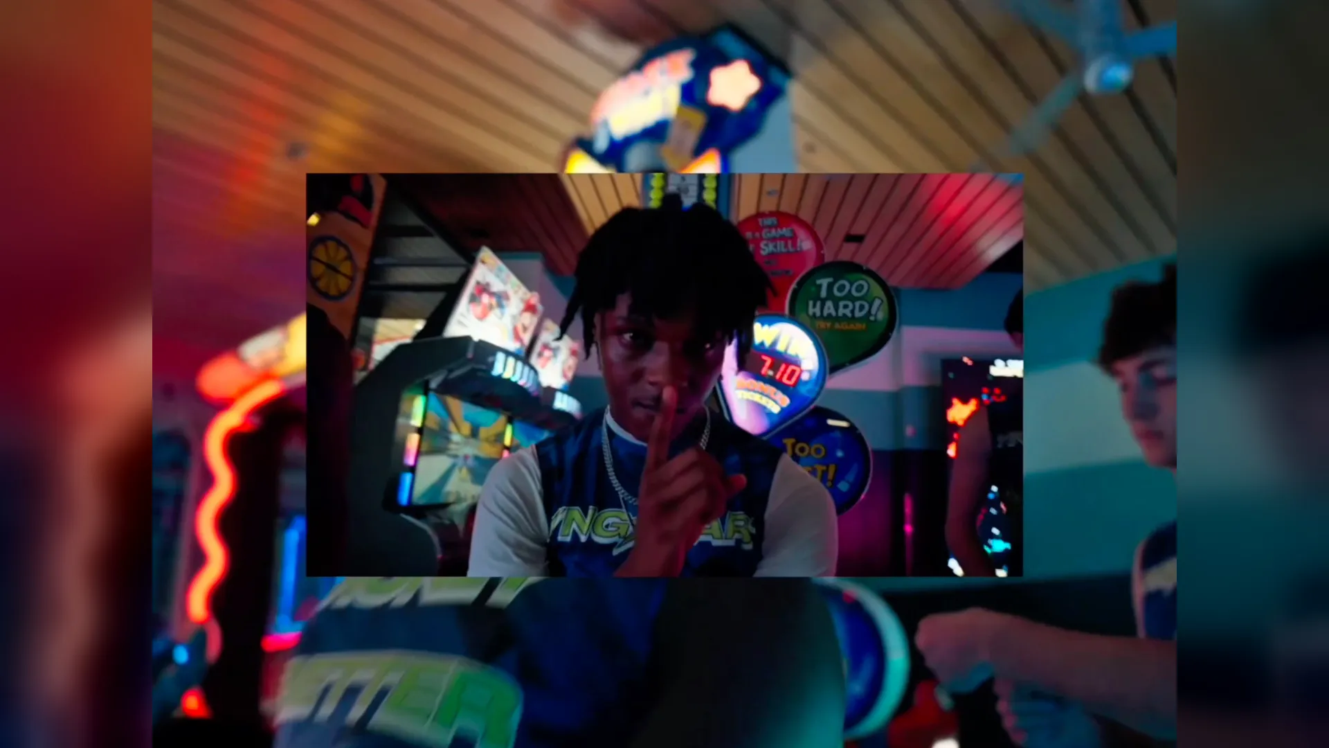 A young athlete in a YNGSTAR jersey holds a finger to his lips in a neon-lit arcade